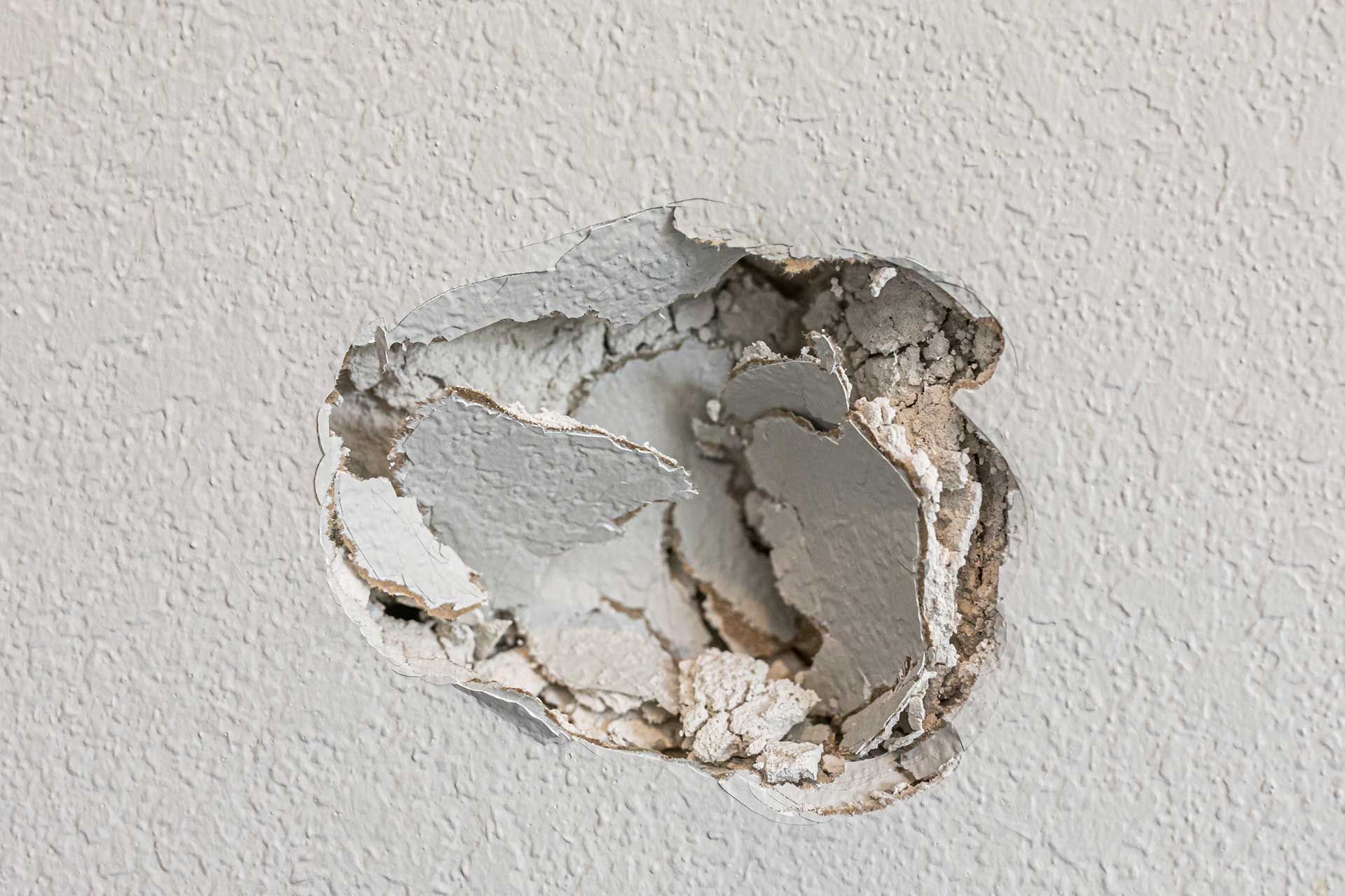 A hole in a white wall with peeling paint and exposed plaster