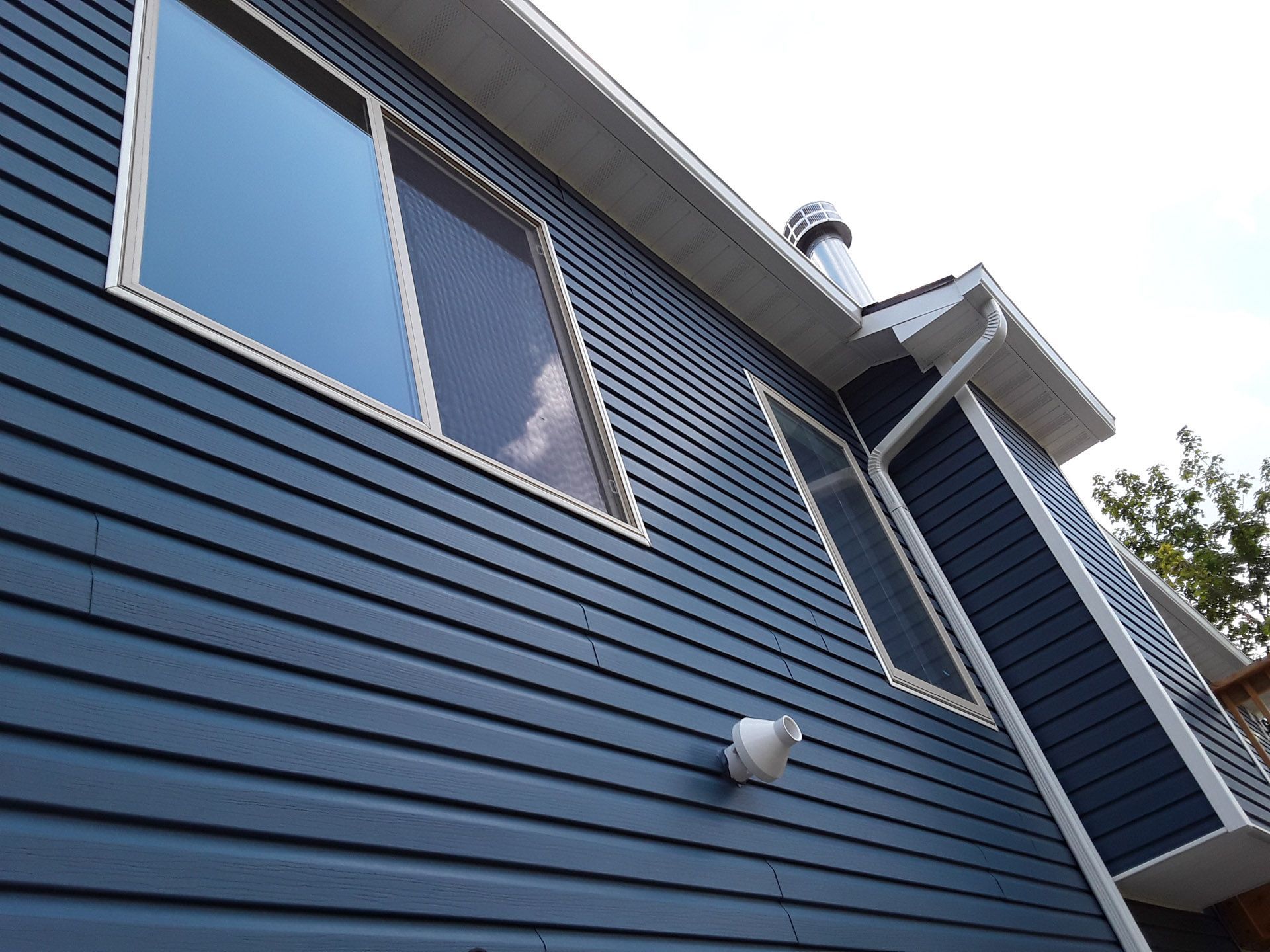 Blue house exterior with horizontal siding and large windows viewed from below