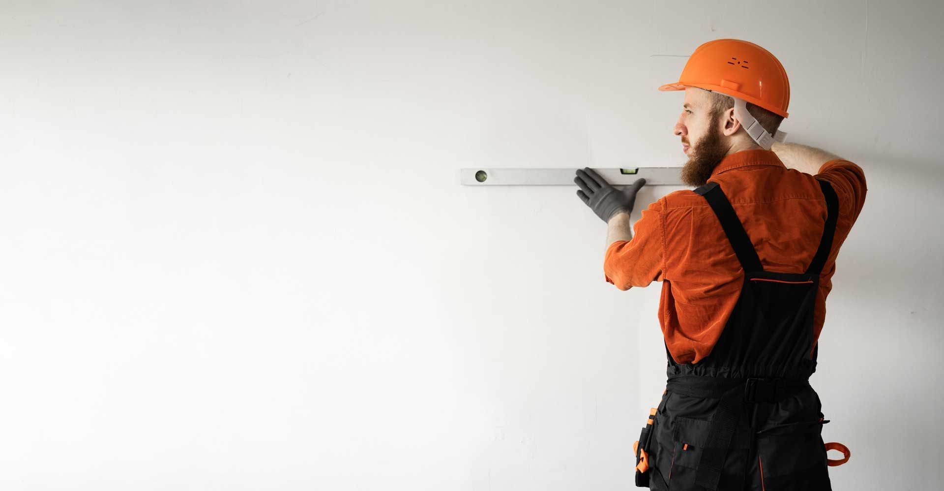 Construction worker in orange hard hat measuring a white wall with a level