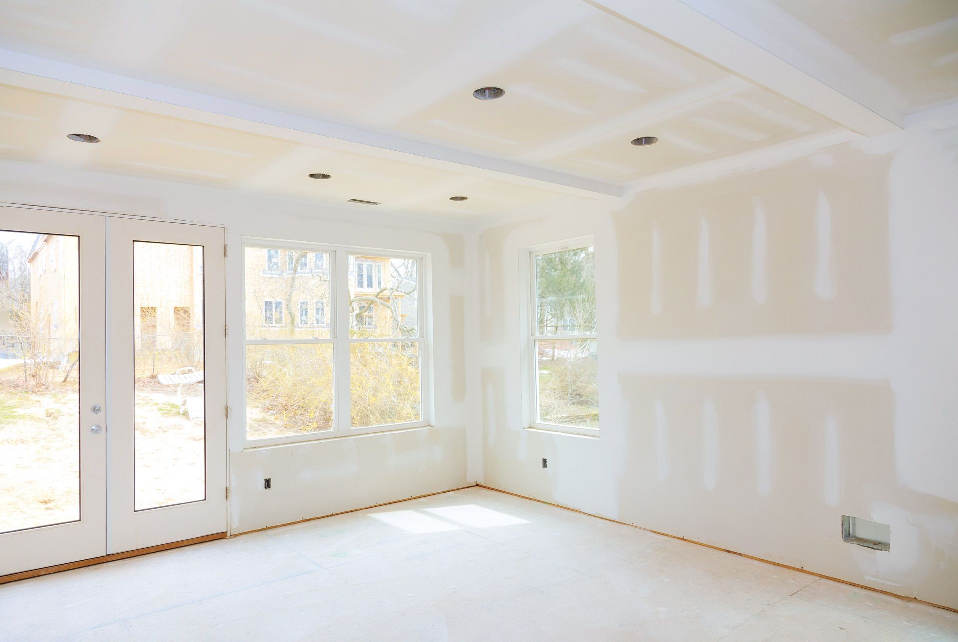 Empty bright room under renovation with white walls, large windows, and French doors