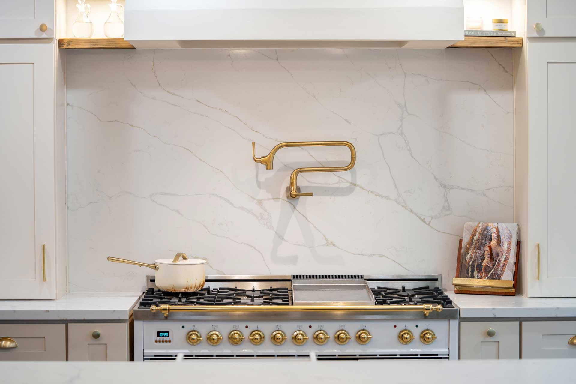 Modern kitchen with white marble backsplash, brass faucet, and stainless steel stove under a hood