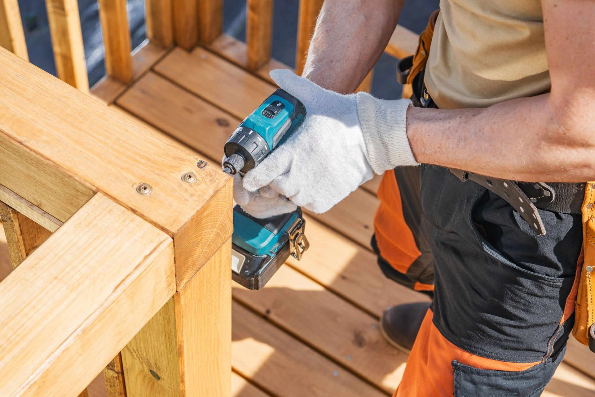 Worker using a teal drill to fasten a wooden frame on an outdoor deck