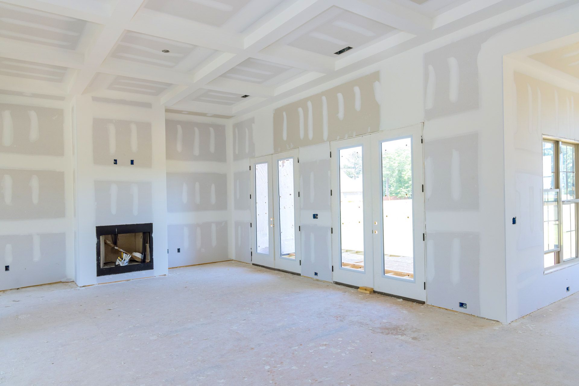 Bright unfinished living room with white drywall, a fireplace, and large glass doors opening outside
