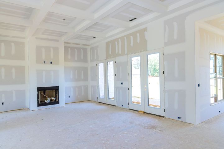 Bright unfinished living room with white drywall, fireplace, and large windows overlooking a yard