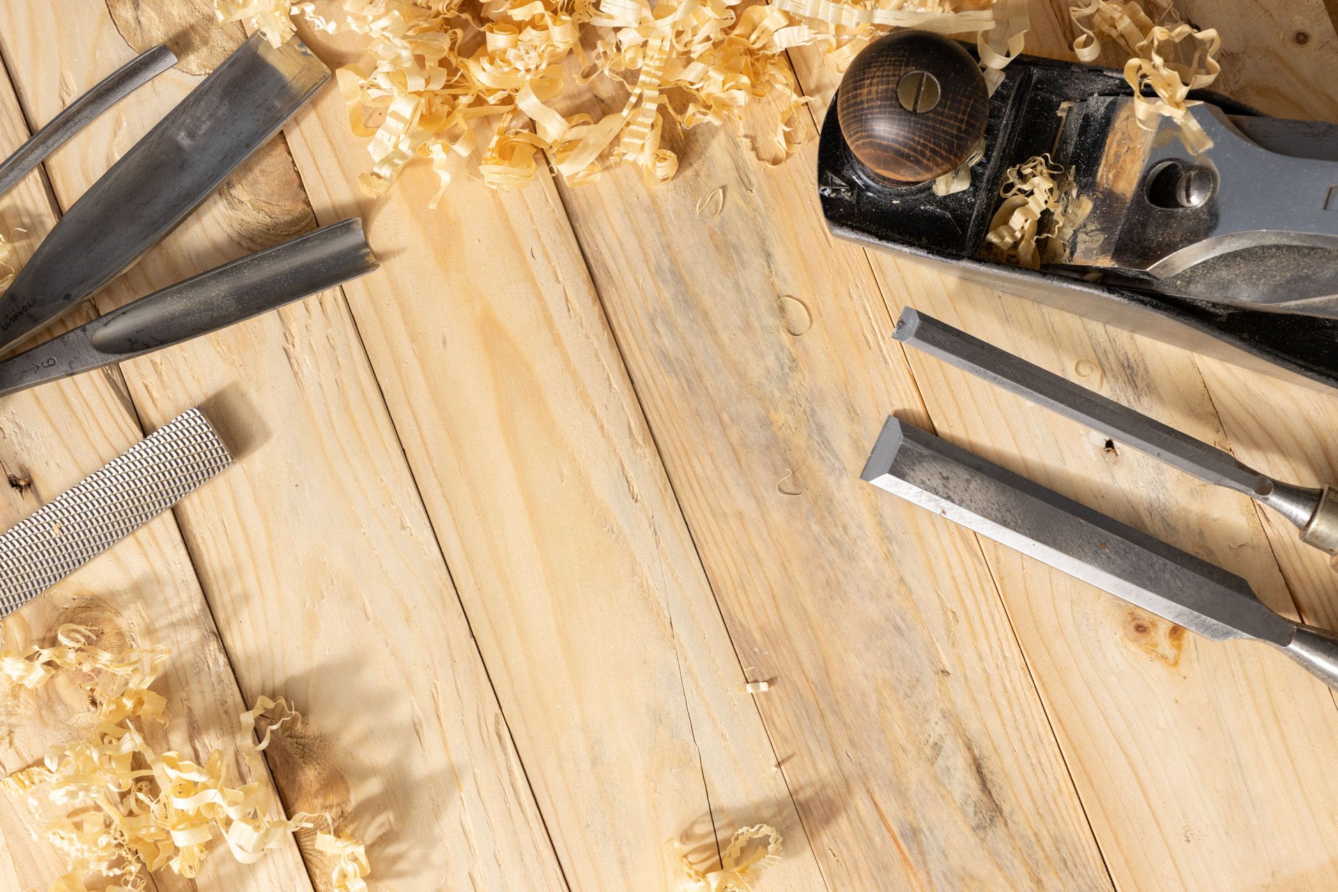 Woodworking tools and wood shavings on a light wooden workbench, including a plane and chisel blades.