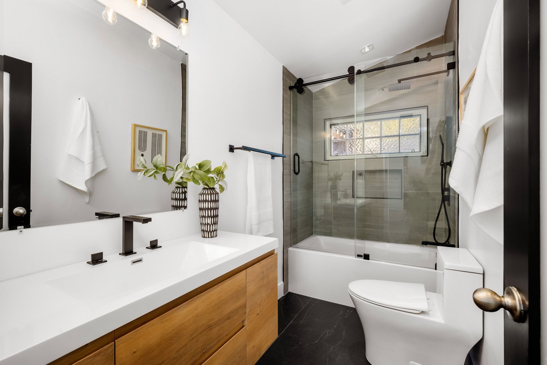Modern bathroom with white vanity, black fixtures, glass shower, and wooden cabinet accents