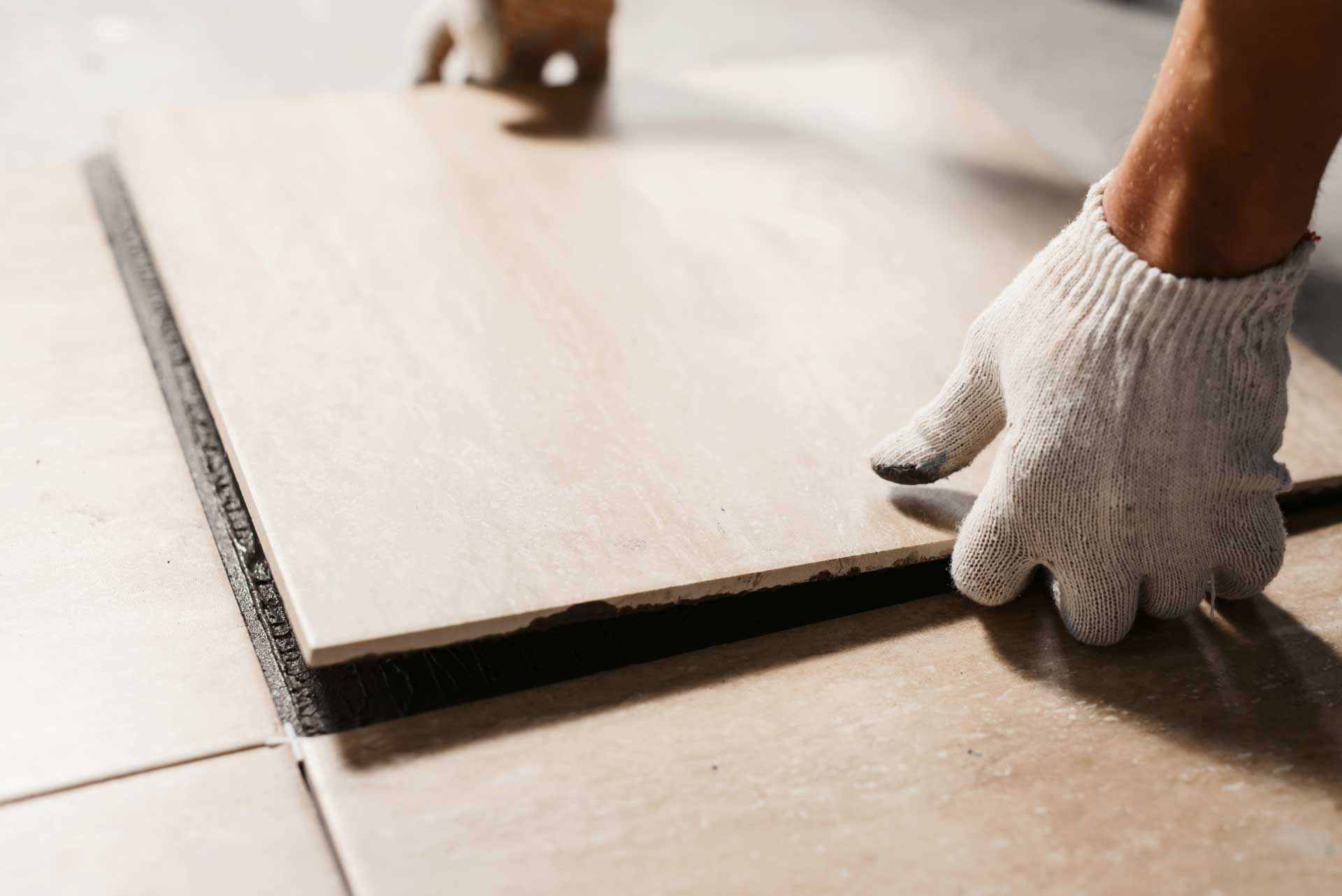 Gloved hands laying a light wood floor plank on a tiled surface