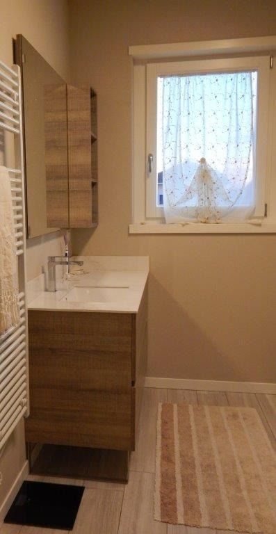 Piccolo bagno con mobiletto in legno, lavabo bianco.