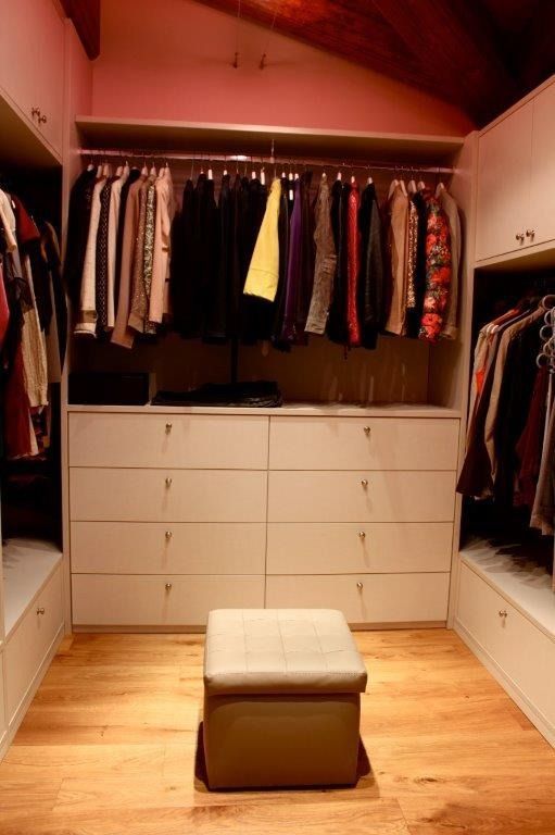 Cabina armadio con abiti appesi, cassetti bianchi e un piccolo pouf.