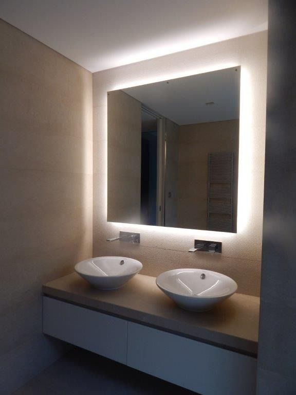 Mobile bagno moderno con due lavabi a ciotola e specchio retroilluminato in tonalità neutre.