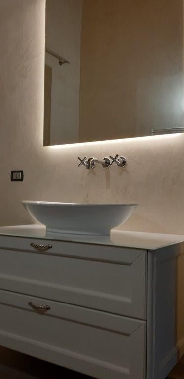 Mobile bagno moderno con lavabo rotondo, specchio e rubinetteria a parete in tonalità neutre.