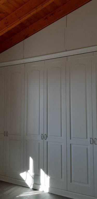 Armadi a muro bianchi con ante integrate, sotto un soffitto di legno inclinato.