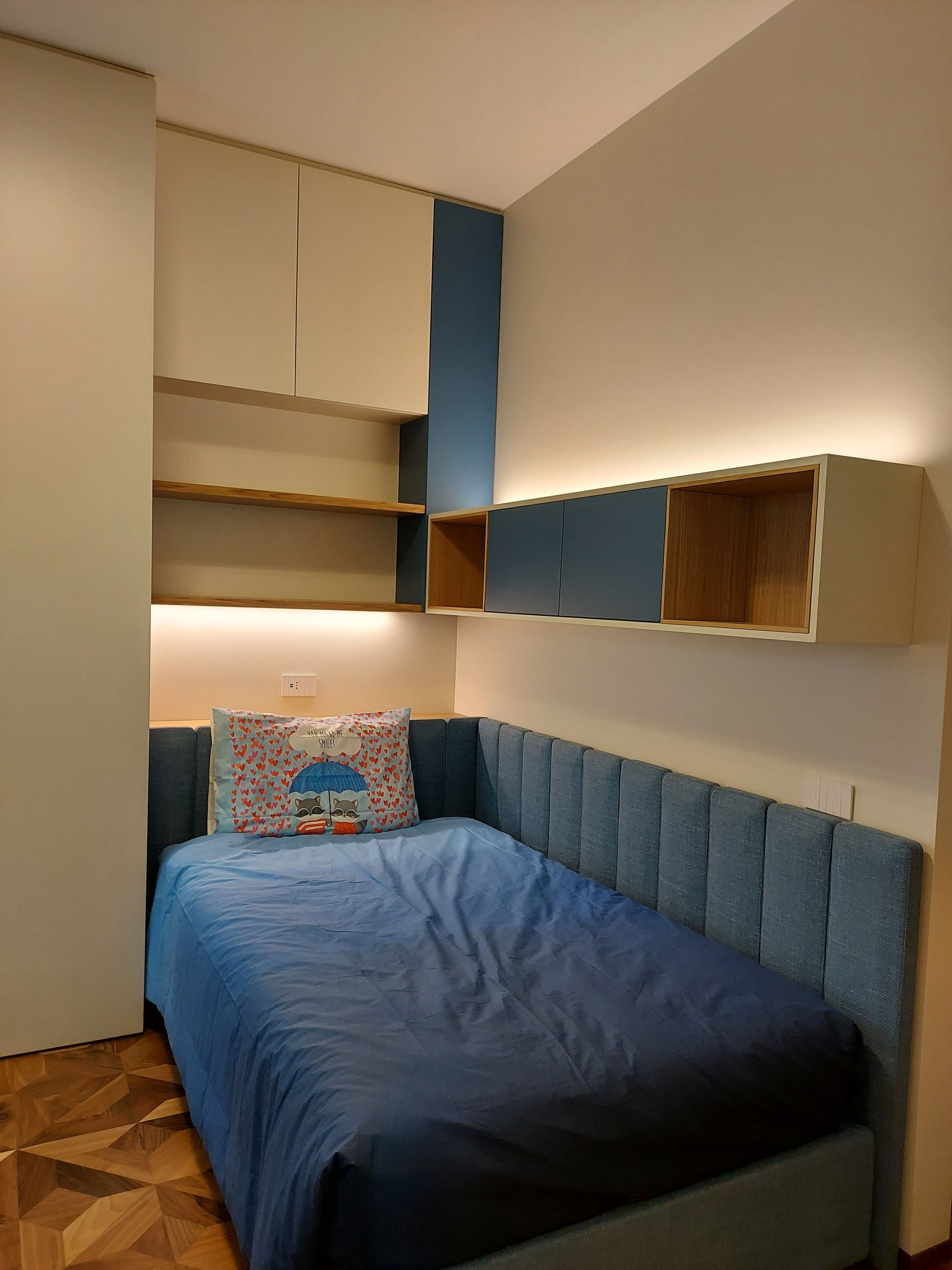 Piccola camera da letto con letto blu, armadi a muro e illuminazione calda sotto i ripiani.