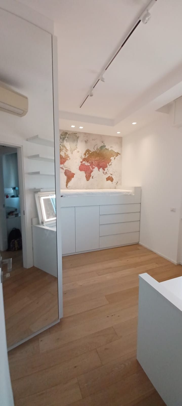 Camera da letto moderna e luminosa con comò bianco, mappa a parete e anta dell'armadio a specchio.
