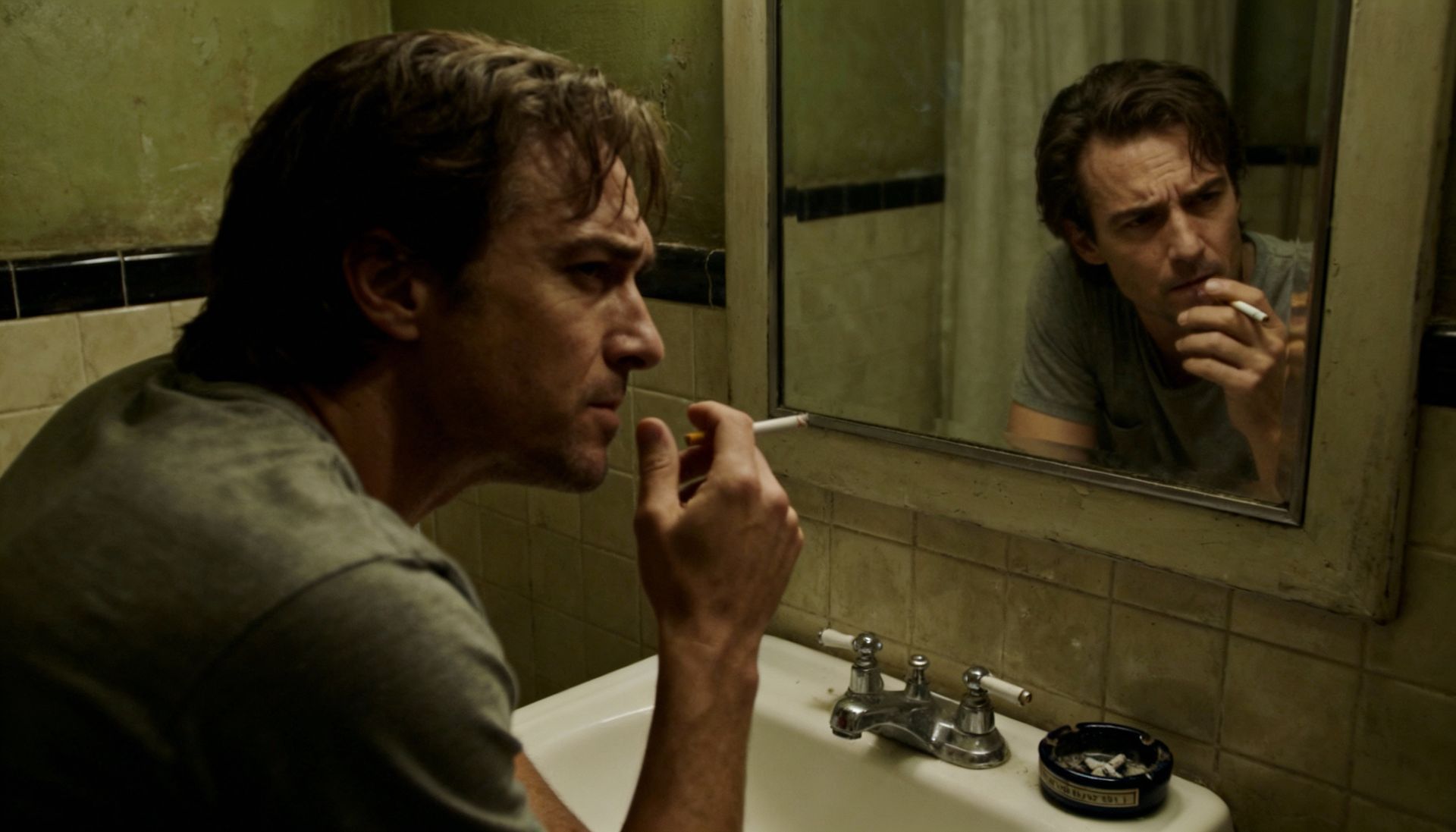 Man looking in the mirror with a conflicted expression, holding a cigarette, ashtray on sink
