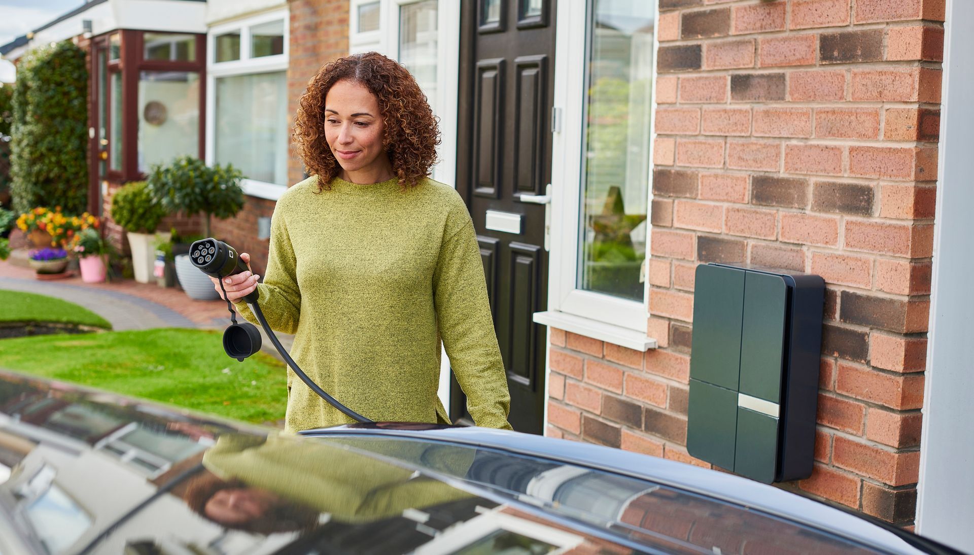 A woman holding an electric vehicle charging cable outside a house.