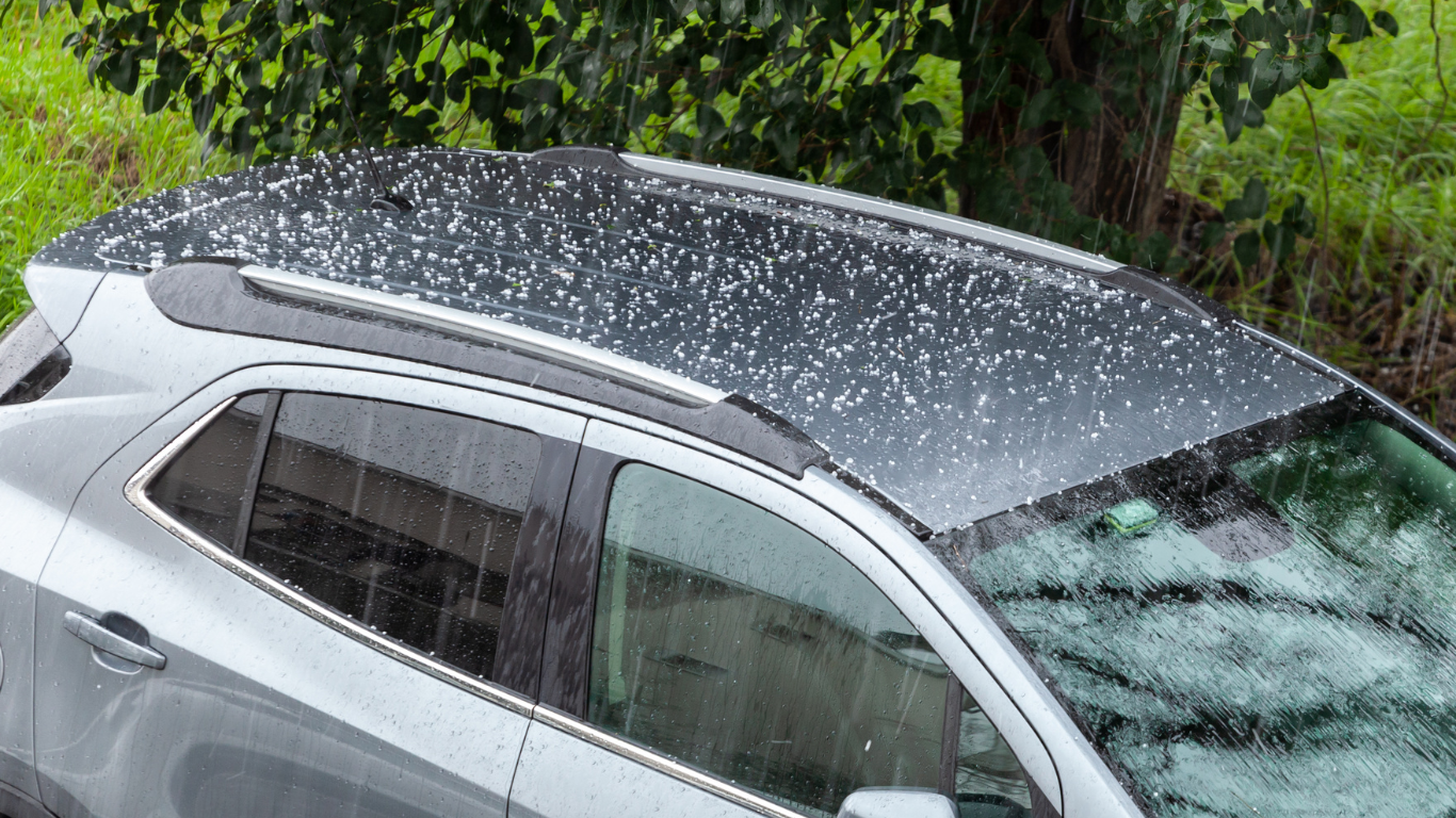 A car with hail on the roof is parked in the rain.