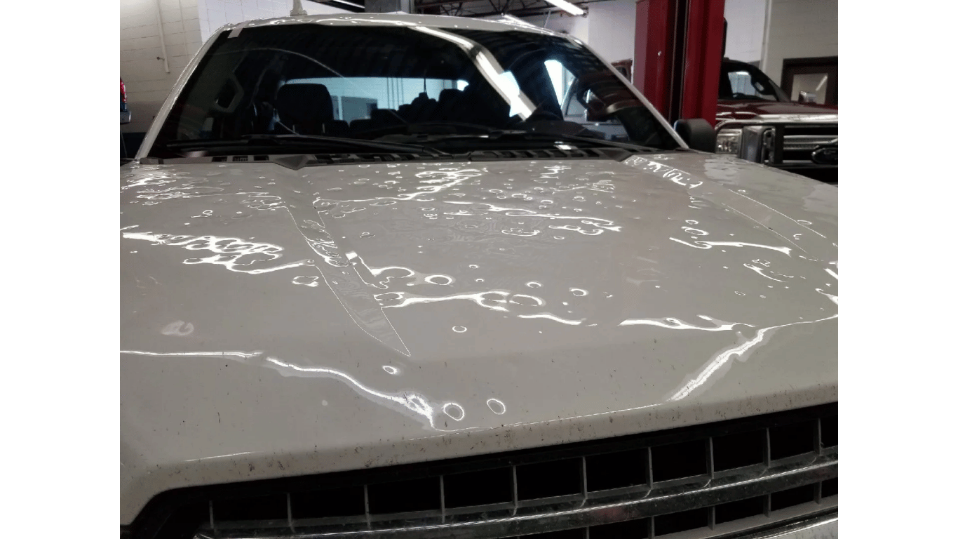 The hood of a white car is covered in hail.