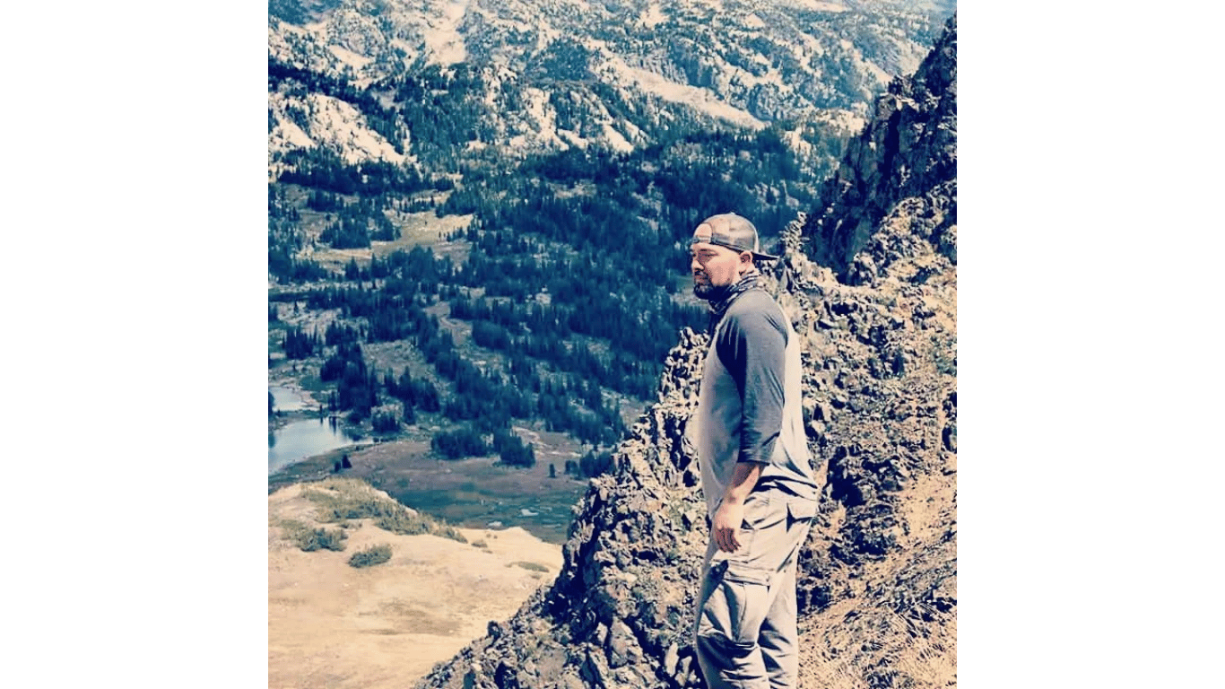 A man is standing on top of a mountain looking out over a valley.