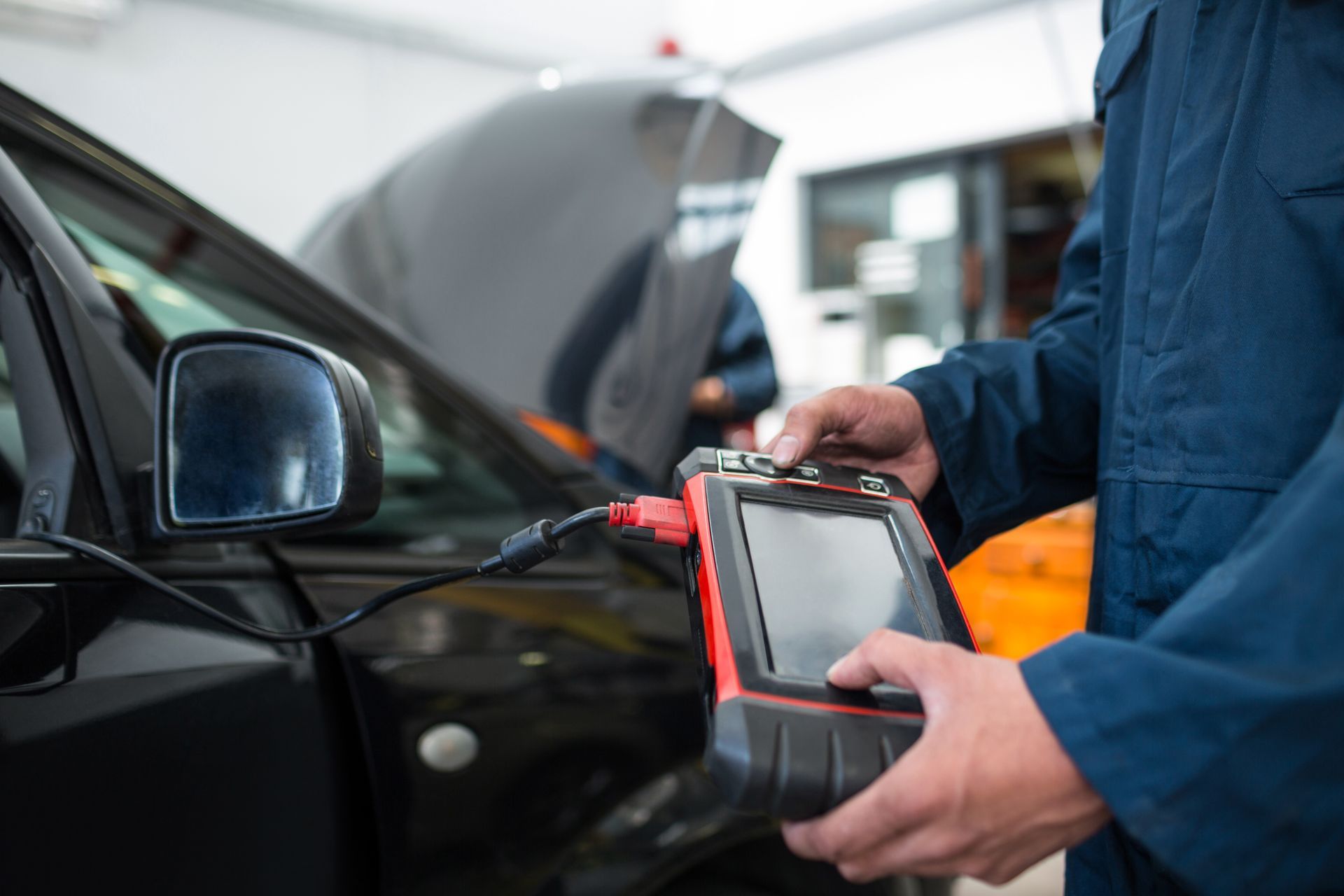 Close-up of a mechanic using a diagnostic tool on a black car at a repair garage.