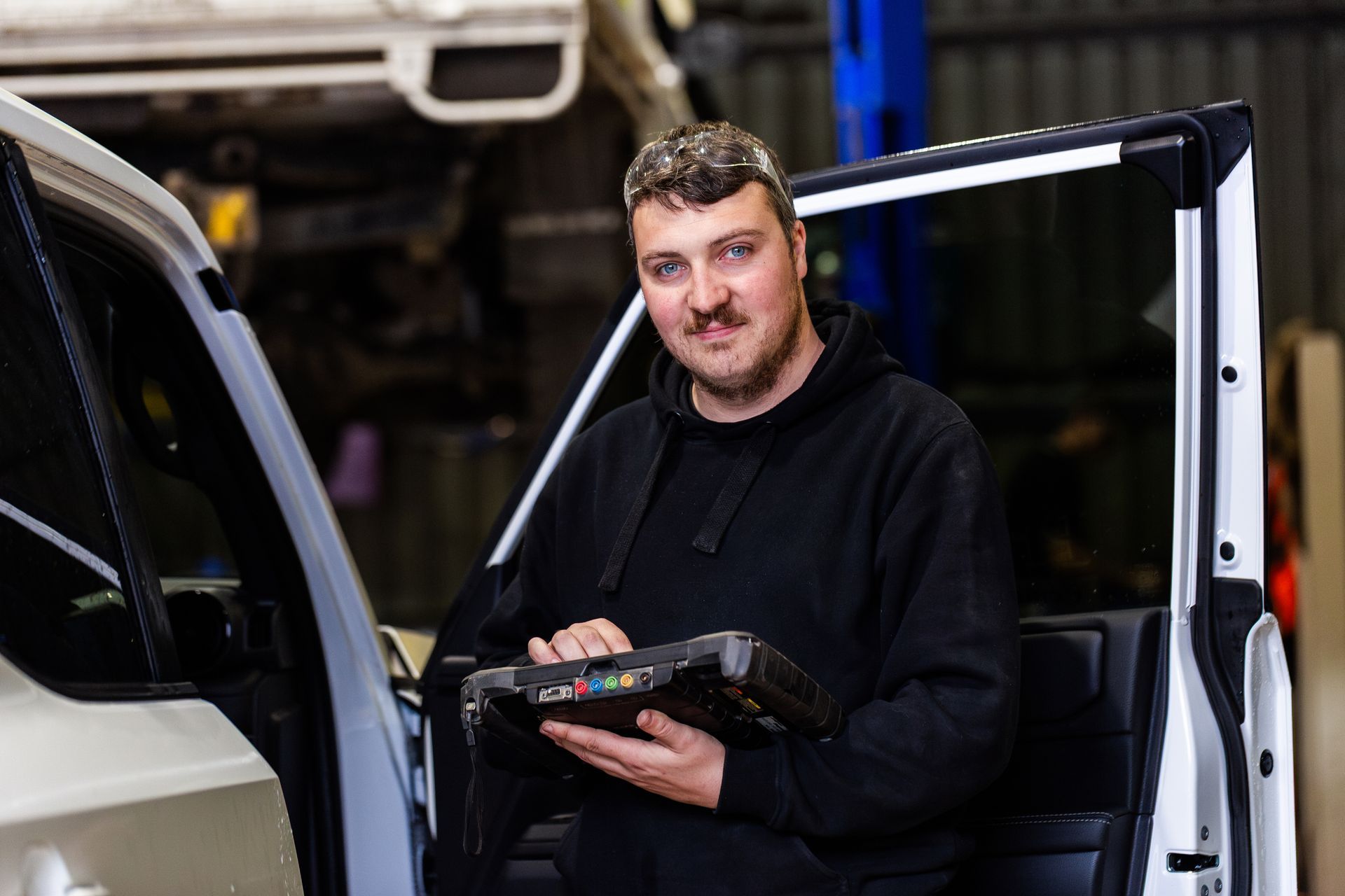 Car mechanic with diagnostic device testing a vehicle in a workshop.