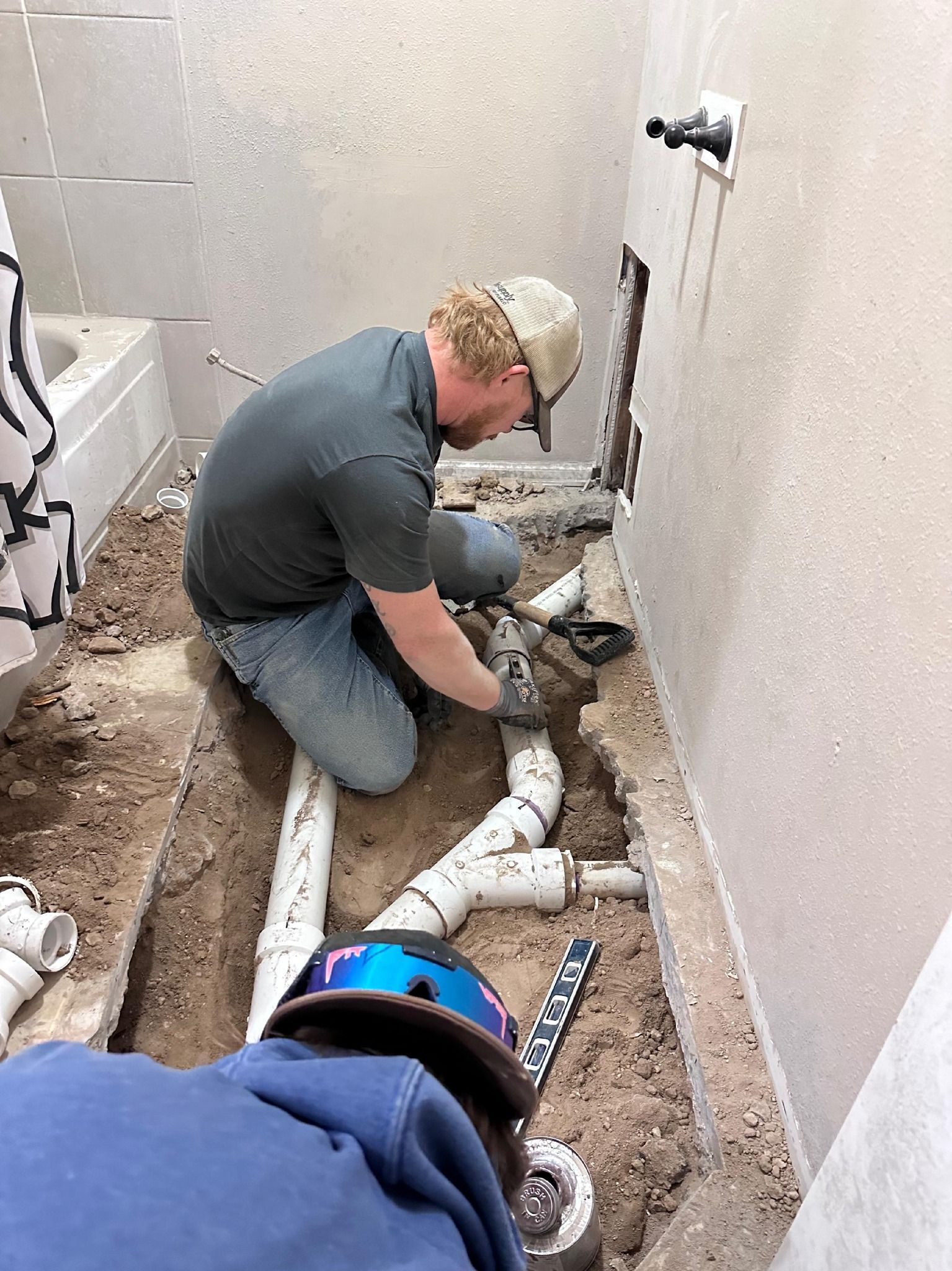 Two people working on plumbing in a bathroom, near a bathtub. One person kneels, connecting pipes.
