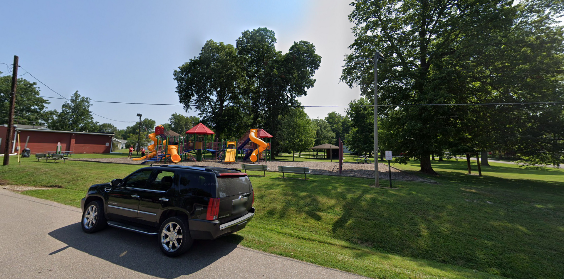 Workers in orange vests on a roadside crew truck near a grassy park with trees.