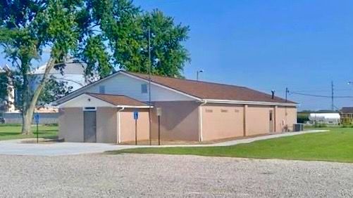 Single-story tan brick building with a white entrance, gravel lot, and blue sky