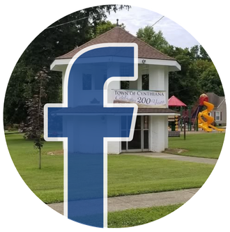 Blue Facebook logo over a town sign and building in a grassy park setting