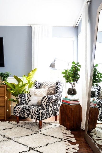 A living room with a chair , ottoman , rug and mirror.