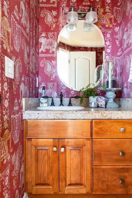 A bathroom with a sink , mirror and red wallpaper.