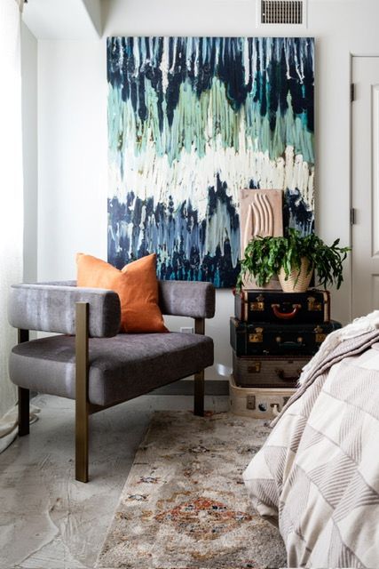 A bedroom with a chair and a large painting on the wall.