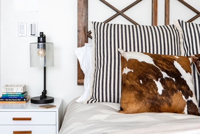 A bedroom with a bed , nightstand , lamp and cowhide pillows.