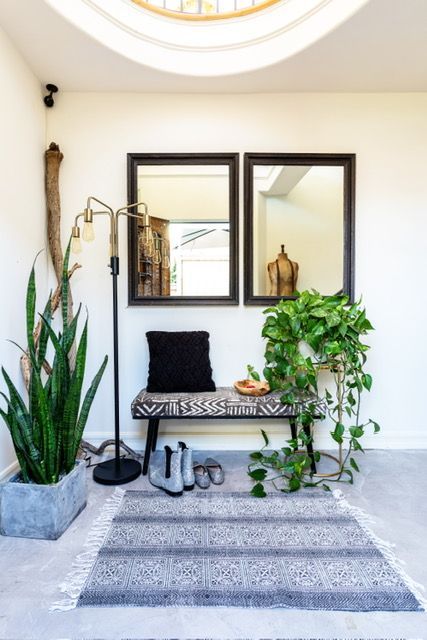 A hallway with a bench , mirrors , plants and a rug.