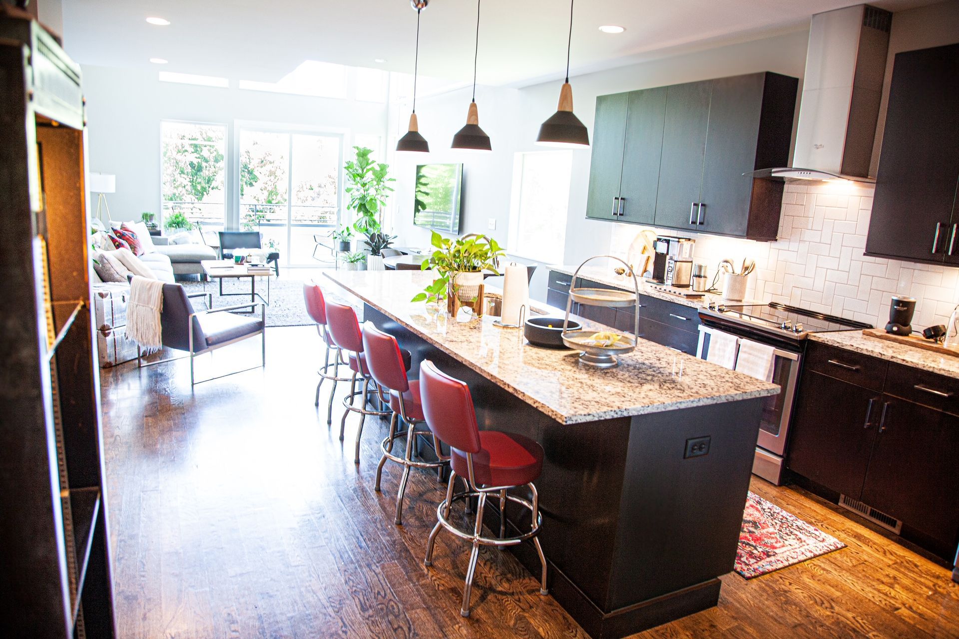 A kitchen with a large island and stools and a living room in the background.