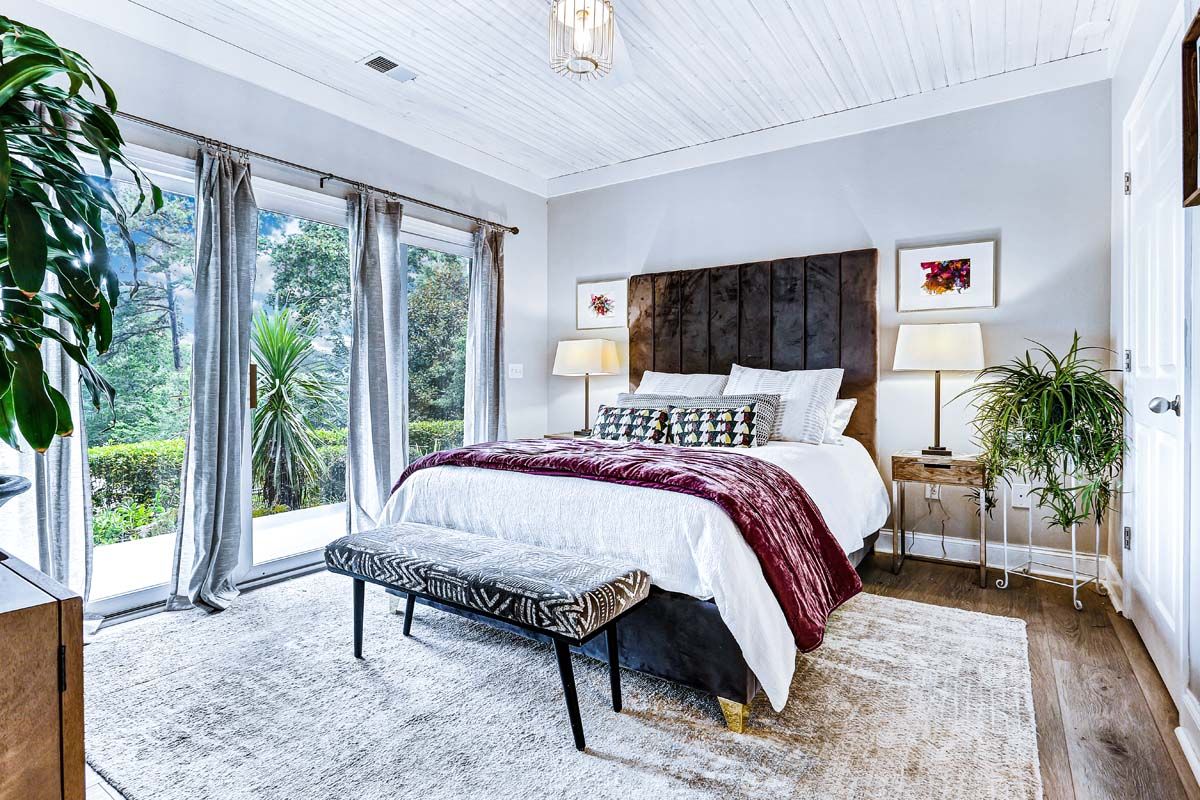 A bedroom with a bed , bench , lamps , and a large window.