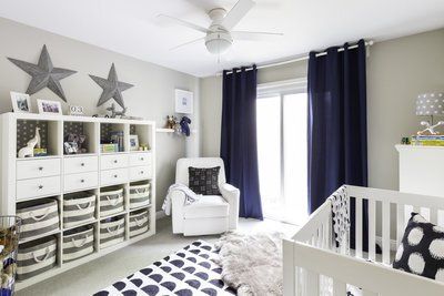 A nursery with a crib , chair , shelves and a ceiling fan.