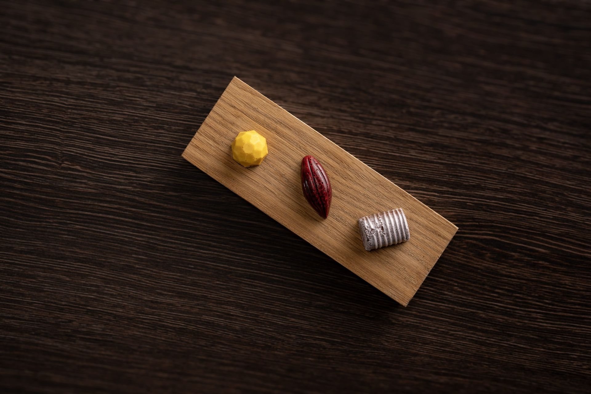 Three chocolates are sitting on a wooden tray on a wooden table.