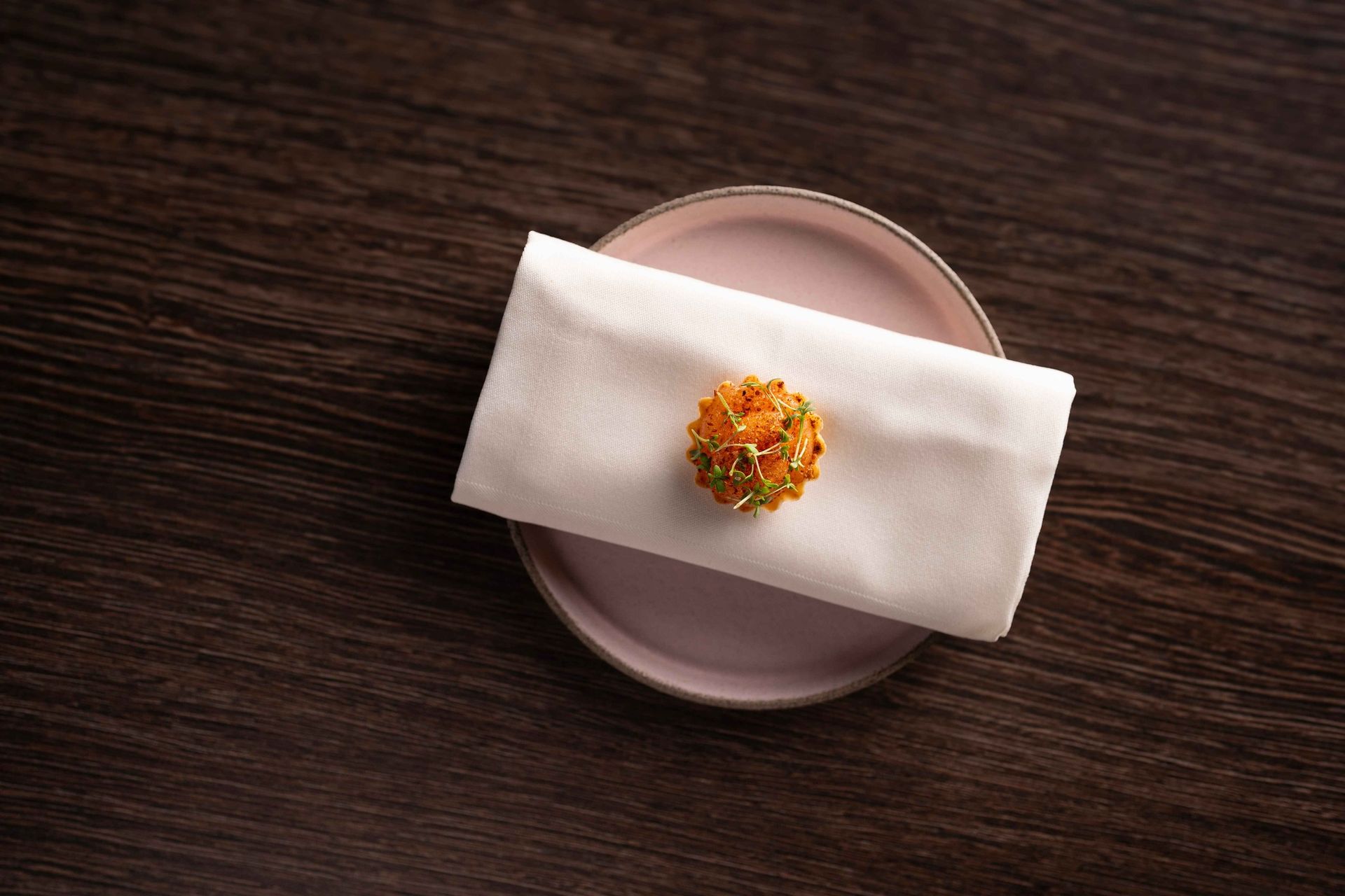 A napkin is sitting on a pink plate on a wooden table.