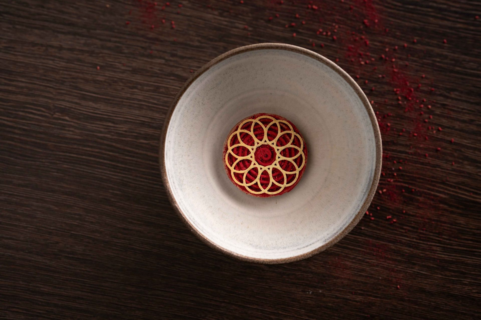 A white bowl with a red flower on it is on a wooden table.