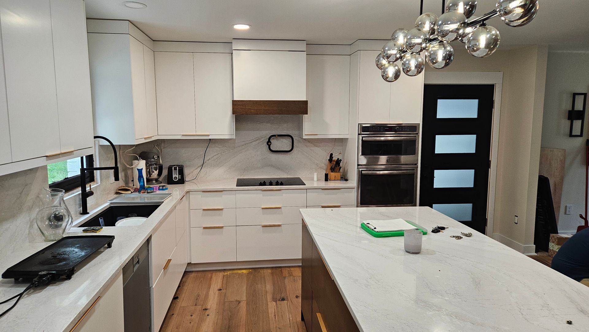 Modern white kitchen with island, pendant lights, wooden floor, black stove, and built-in oven