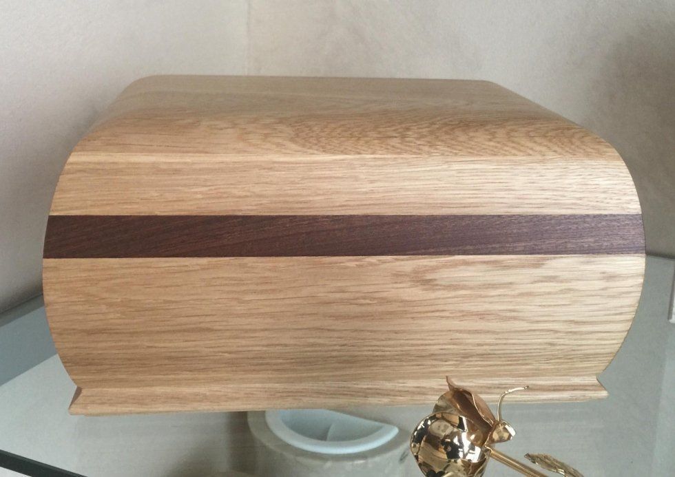 Scatola di legno con parte superiore curva e striscia decorativa marrone scuro.