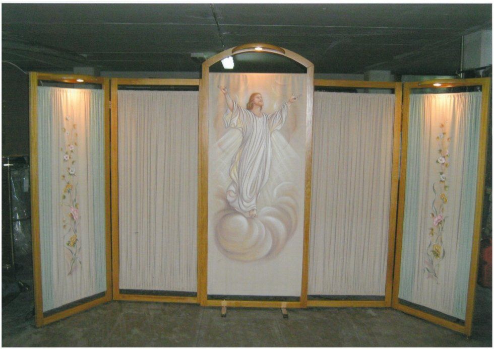 Opera d'arte religiosa raffigurante Gesù su una nuvola, incorniciato da pannelli con motivi floreali e illuminato da faretti.