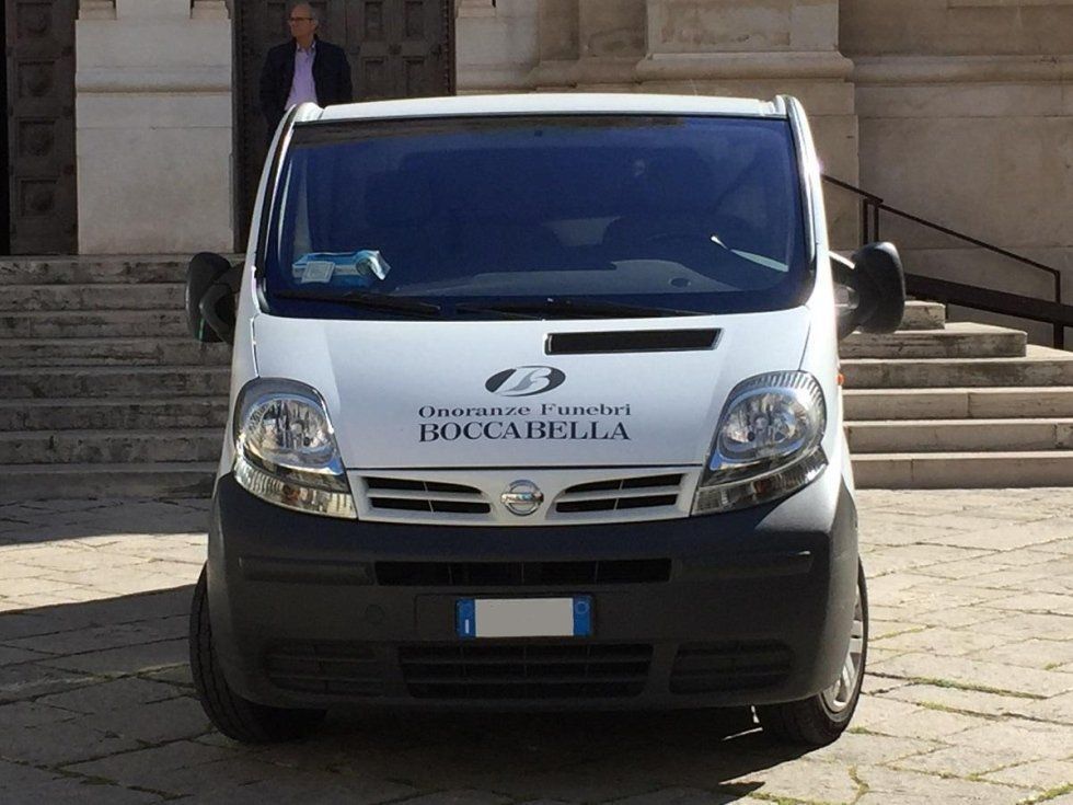 Un furgone Nissan bianco parcheggiato fuori da un edificio; sullo sfondo c'è un uomo.