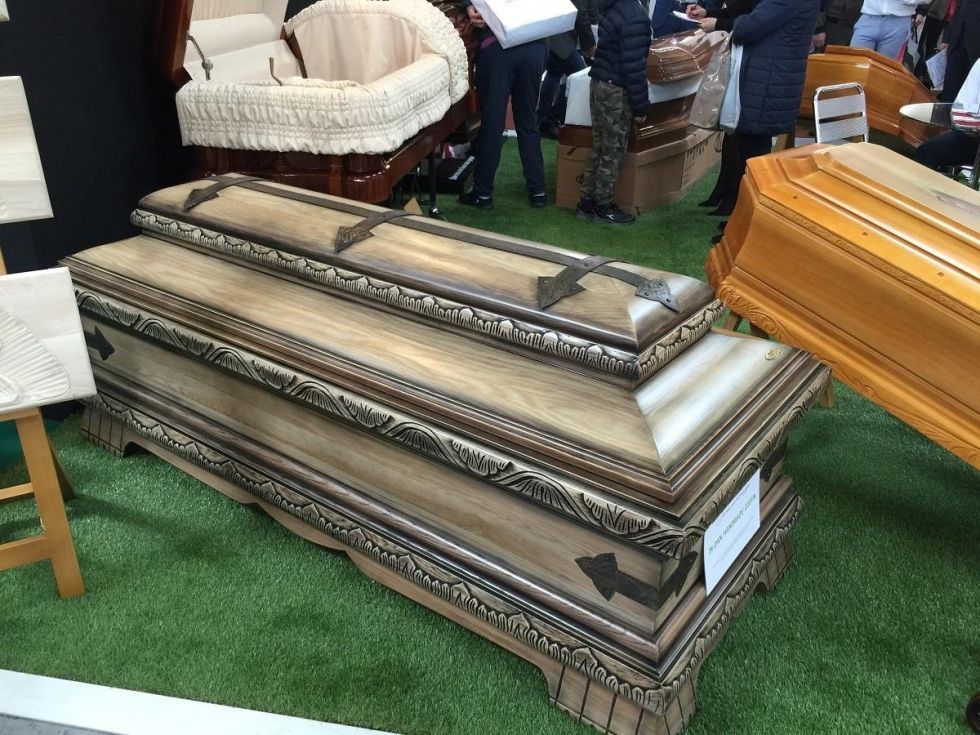 Bare di legno esposte in una mostra, visibili vari stili e colori, adagiate su erba artificiale.