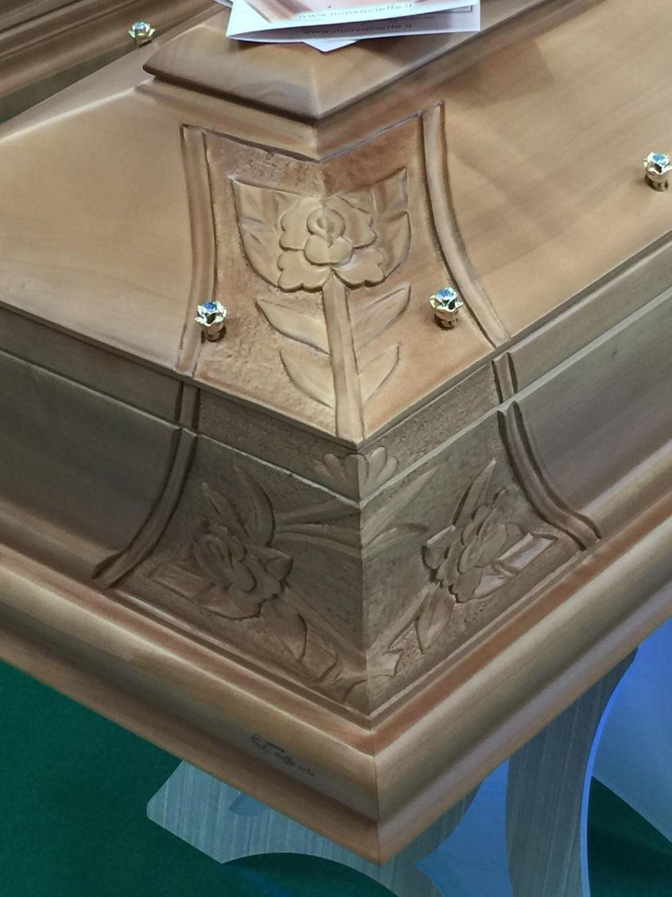 Primo piano dell'angolo di una bara in legno con motivo floreale intagliato e dettagli in pietre preziose blu.