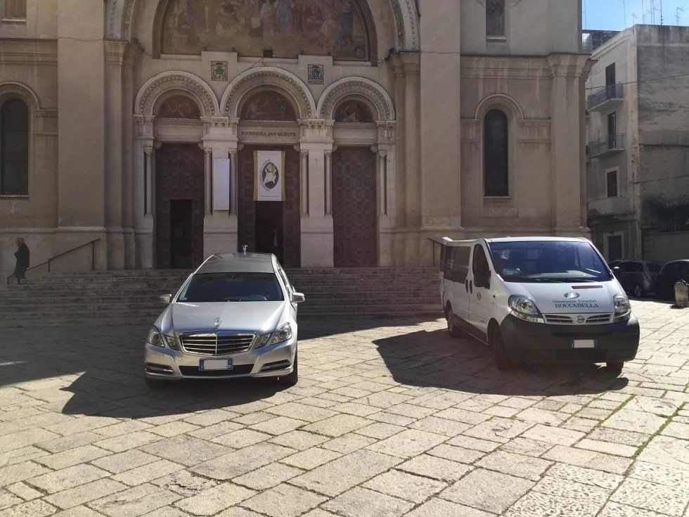 Un carro funebre e un furgone parcheggiati fuori da una chiesa con una facciata in pietra.