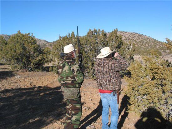 A man in a camo jacket stands next to a man in a cowboy hat