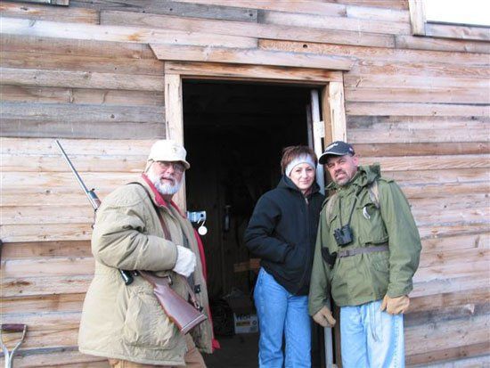 Three people are standing in front of a wooden building