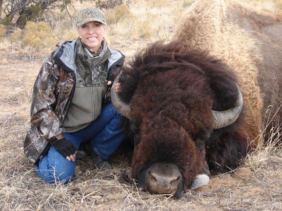 A woman is kneeling next to a large bison
